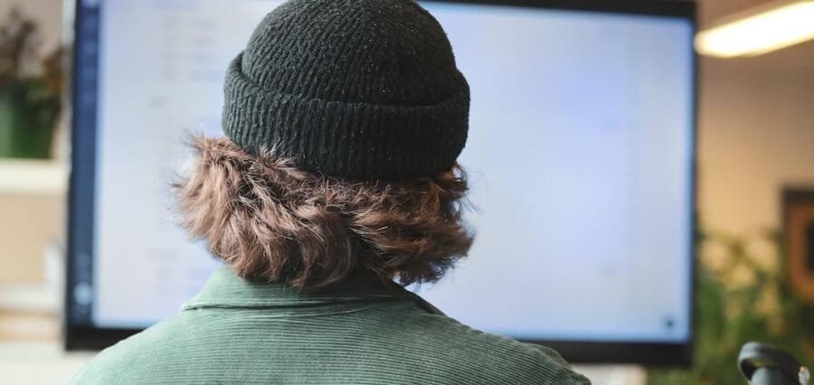 A man with a beanie looks over data on a monitor